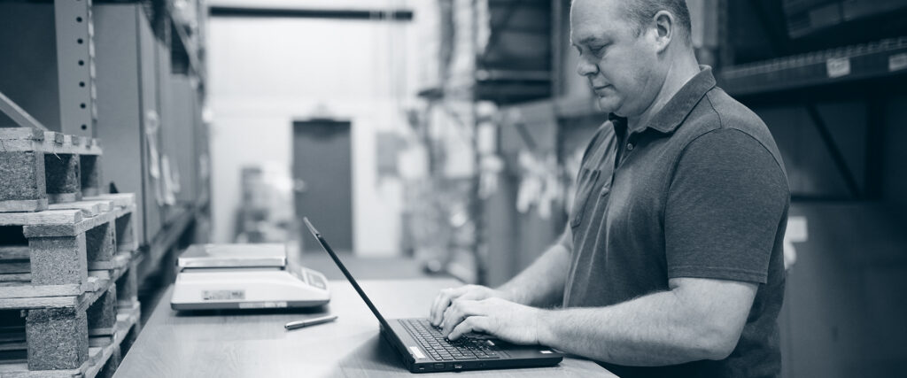 Mann på PC i fabrikk/lager.